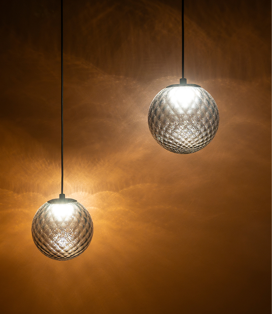 Deux luminaires suspendus en verre texturé, diffusant une Electricité douce sur un mur ocre.